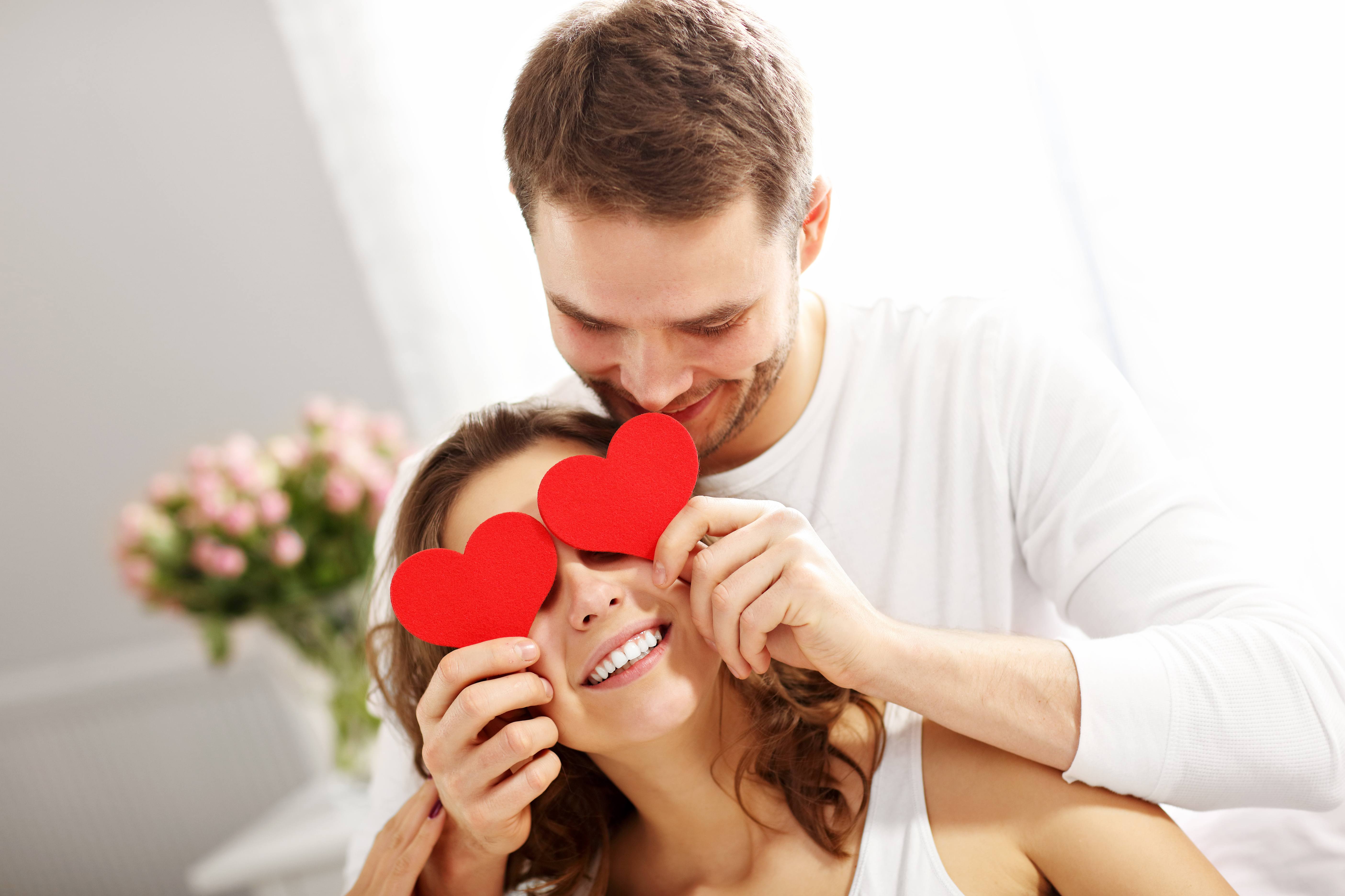 Man holding heart shaped card in front of woman's eyes