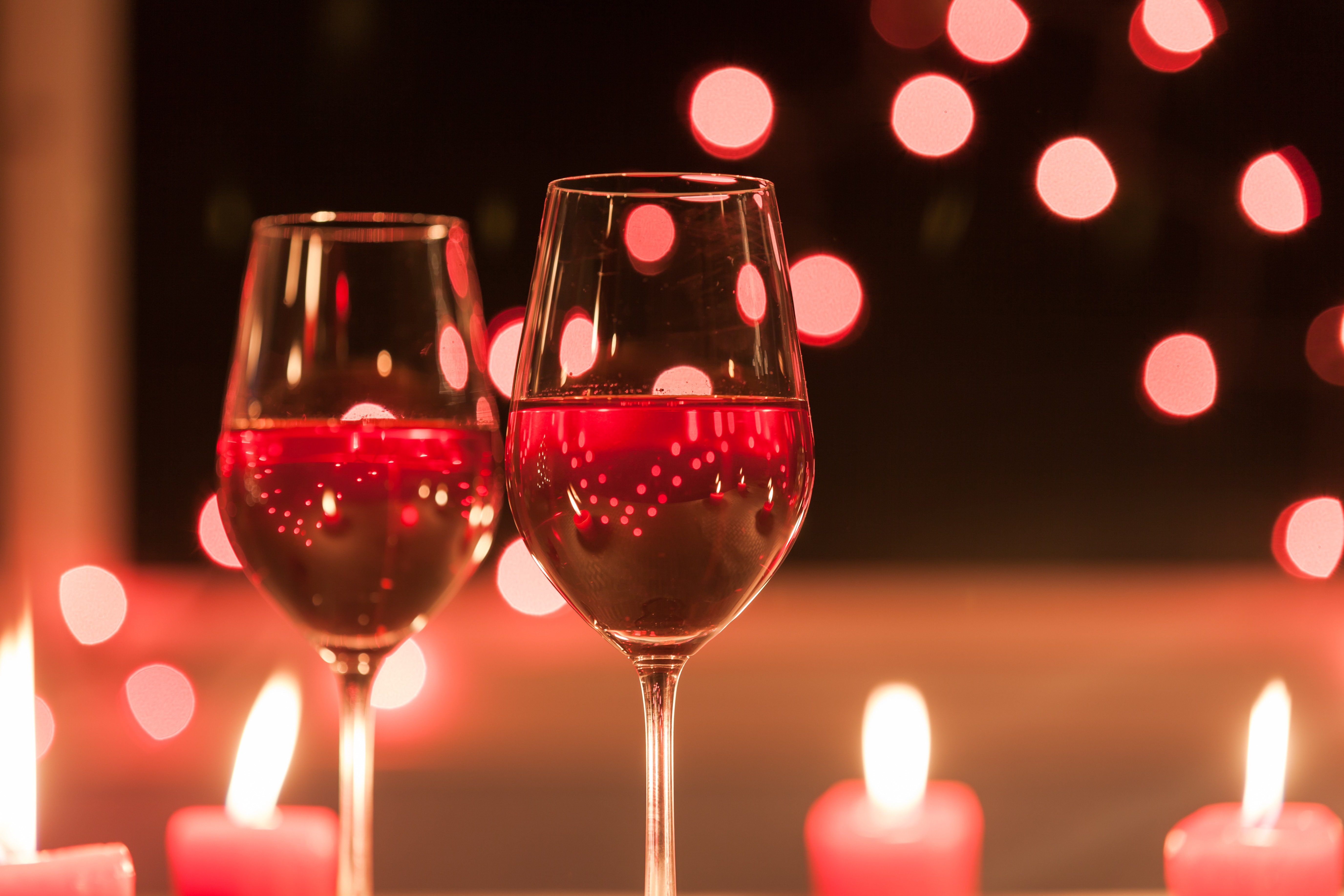 Two wine glasses with candles in background 